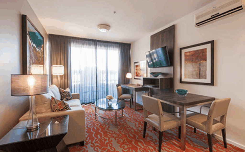 Bright hotel suite with red patterned carpet and sitting area.